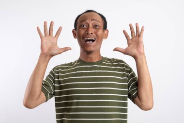 Beyaz çizgili yeşil tişört giyen Asyalı bir adam iki elini birden kaldırıyor, parmakları açık, şaşkınlık ve neşe ifadesi ile. Fotoğraf düz beyaz bir arkaplana göre ayarlandı