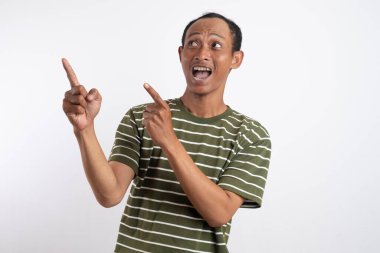 Yeşil tişörtlü Asyalı bir adam, sanki bir reklam aracı için beklenmedik bir şey fark ediyormuş gibi, şaşırmış ve meraklı bir ifadeyle yan tarafı işaret ediyor. Beyaz arka plan onun heyecanlı ifadesini vurguluyor..