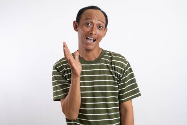 Beyaz çizgili yeşil gömlek giyen Asyalı bir adam geniş ağızlı bir gülümseme ile coşkuyla dalgalanır, açık gri bir stüdyo arka planına karşı durur. Onun neşeli ifadesi heyecan ve dostluğu iletir.