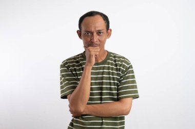 Yeşil tişörtlü genç bir Asyalı eli çenesinde ve kolları çapraz bir şekilde dimdik ayakta duruyor.