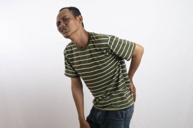 Beyaz çizgili yeşil tişört giyen Asyalı adam sinir ağrısı ve acı ifadesi nedeniyle kalçasını tutuyor. kalça kemiği sağlığı kavramı.