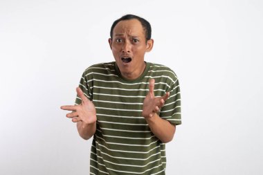 Beyaz çizgili yeşil gömlek giyen Asyalı bir adam kafası karışık ve belirsiz bir ifadeyle omuz silkiyor, kolları açık ve avuçları havada. Açık mavi arka plan, onun muğlak...