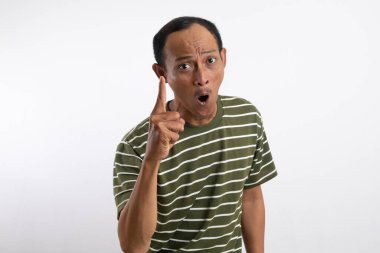 Ciddi bir ifadeye sahip beyaz çizgili yeşil gömlek giyen Asyalı bir erkek işaret parmağını yukarı kaldırıyor. Sanki bir uyarı veriyormuş ya da önemli bir noktaya parmak basıyormuş gibi. Açık mavi arkaplan vurgular