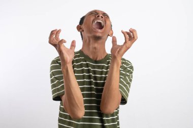 Beyaz çizgili yeşil gömlek giyen Asyalı bir adam kızgın bir ifade sergiliyor, dişlerini gösteriyor ve ellerini pençe gibi hareketlerle kaldırıyor, sanki öfke ya da hüsran içindeymiş gibi. Sade beyaz arkaplan konuyu vurgular.