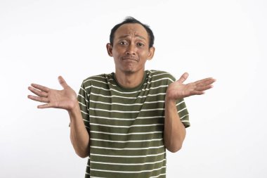 Beyaz çizgili yeşil gömlek giyen Asyalı bir adam kafası karışık ve belirsiz bir ifadeyle omuz silkiyor, kolları açık ve avuçları havada. Açık mavi arka plan, onun muğlak...