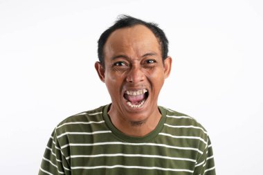 Yeşil tişörtlü Asyalı bir adam, geniş ağzı ve kıvrık gözleri olan yoğun, gürültülü bir yüz ifadesi sergiliyor, sanki bağırıyor ya da aşırı duyguları ifade ediyor gibi, düz beyaz bir arkaplana karşı.