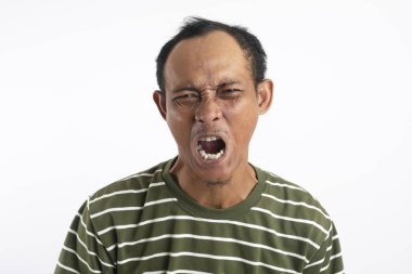 Yeşil tişörtlü Asyalı bir adam, geniş ağzı ve kıvrık gözleri olan yoğun, gürültülü bir yüz ifadesi sergiliyor, sanki bağırıyor ya da aşırı duyguları ifade ediyor gibi, düz beyaz bir arkaplana karşı.