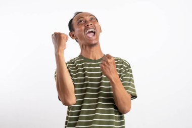 Beyaz çizgili yeşil gömlek giyen bir adam kutlama jesti olarak her iki elini de kaldırır, yüzü heyecan ve neşe içinde ışıldar. Açık mavi arka plan onun zafer ve coşkulu ifadesini vurguluyor..