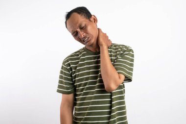 Yeşil gömlek giyen Asyalı bir adam, düz beyaz bir arka plana karşı duruyor, boynunu tutuyor ve rahatsızlık gösteriyor, boyun ağrısını, gerilimi veya gerilimi sıradan bir pozda resmediyor.
