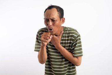 Beyaz çizgili yeşil gömlekli bir adam bir eliyle boğazını, diğer eliyle ağzını kapayarak şiddetle öksürüyor. Onun ifadesi rahatsızlık ve acıyı gösteriyor. Sade açık beyaz arkaplan