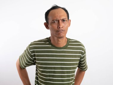 Beyaz çizgili yeşil gömlek giyen ciddi bir adam kameraya yoğun bir şekilde bakıyor ve sert bir yüz ifadesi sergiliyor. Düz beyaz arka plan, onun odaklanmış ve derin düşüncelere dalmış davranışlarını vurguluyor..