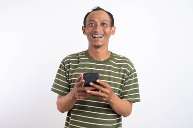 Mutlu hissederken mesaj atmak için akıllı telefon kullanan yeşil tişört giyen neşeli Asyalı genç adam beyaz arka planda izole edilmiş..