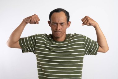 Pozitif Asyalı adamın belden yukarı vuruşu kolunu yukarıda tutuyor. Ne kadar güçlü olduğunu gösteriyor. Gülümsüyor, gururlu bir şekilde beyaz stüdyo arka planında izole edilmiş siyah tişört giyiyor.