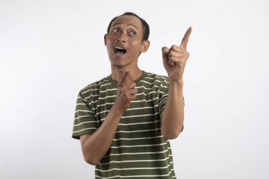 Yeşil tişörtlü Asyalı bir adam, sanki bir reklam aracı için beklenmedik bir şey fark ediyormuş gibi, şaşırmış ve meraklı bir ifadeyle yan tarafı işaret ediyor. Beyaz arka plan onun heyecanlı ifadesini vurguluyor..