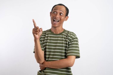 Yeşil tişörtlü Asyalı bir adam, sanki bir reklam aracı için beklenmedik bir şey fark ediyormuş gibi, şaşırmış ve meraklı bir ifadeyle yan tarafı işaret ediyor. Beyaz arka plan onun heyecanlı ifadesini vurguluyor..