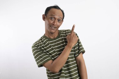 Beyaz çizgili yeşil tişört giyen bir adam sanki bir fikri varmış gibi işaret parmağı havada yukarı bakıyor. Onun ifadesi hareketli ve coşkulu. Açık mavi arka plan onun enerjisini vurguluyor.