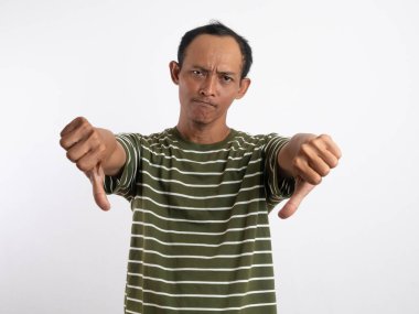 Beyaz çizgili yeşil tişört giyen bir adam hoşnutsuzluğunu veya memnuniyetsizliğini belirtmek için dilini uzatan hoşnutsuzluğunu gösteren hoşnutsuzluğunu gösteren bir hareket sergiliyor. Sade açık mavi arkaplan