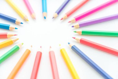 Renkli kalemler dairesel bir çerçeve oluşturarak sol üstte, beyaz arkaplanda metin için boşluk oluştururlar. Öğrenim, çocuk ve oyuncu tasarım başlıkları için yaratıcı, eğitici ve sanatsal bir düzen.