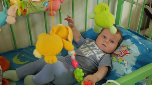 Babyjongen liggend In bedje met speelgoed — Stockvideo