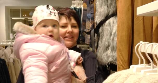 Женщина с ребенком выбирает одежду во время покупок — стоковое видео