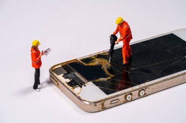 Parlak turuncu elbiseli iki minyatür işçi alet kullanarak kırılmış bir akıllı telefon ekranını tamir ediyor. Cihaz üzerinde dikkatlice değerlendirip çalışıyorlar..