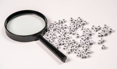 Bir büyüteç düz bir yüzeyde beyaz harf bloklarının yanında duruyor. Her blok, eğlenceli bir öğrenme sahnesi yaratan tek bir siyah harf içeriyor..