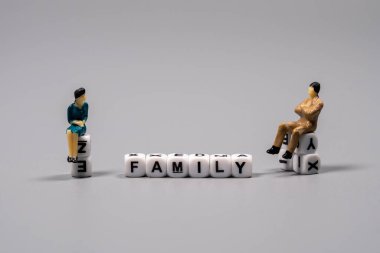 Harflerin her iki tarafında oturan iki küçük figür aile ilişkileri ve bağlantıları hakkında bir tartışmayı sembolize ediyor..