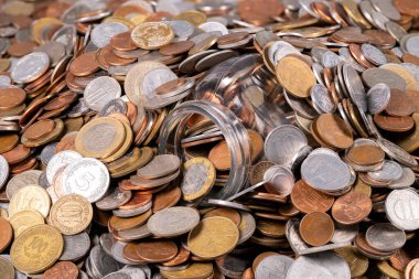 Masaya çeşitli madeni paralar serilir, ortada cam bir kavanoz ters çevrilir ve etrafa saçılmış para birimleri ışığı yansıtır..