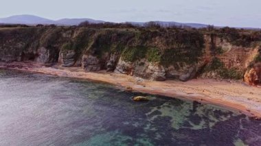 Bu çarpıcı manzara, Bulgaristan 'ın kıyılarında hafif dalgaların dalgalandığı kayalık bir kıyı şeridini gösteriyor. Bereketli yeşillik açık bir gökyüzünün altında kumlu plajlarla buluşur..