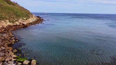 Bulgaristan 'ın kayalık kıyı şeridini görüntüleyen bir hava perspektifi, berrak mavi suları ve uzaktan görülebilen bir deniz feneriyle hafif dalgaları gösteriyor..