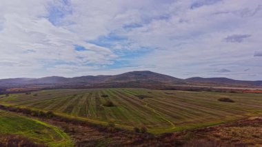 Bulgaristan 'ın sonbahar mevsiminde kırsal kesiminin doğal güzelliğini gözler önüne seren bulutlu bir gökyüzü altında geniş araziler boyunca uzanır..