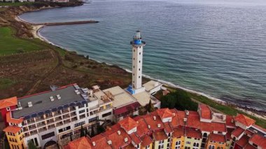 Bu hava sahnesi, Bulgaristan 'ın güzel manzarasını vurgulayan renkli binalar ve sakin denizlerle çevrili bir kıyı şeridi yakınında uzun bir deniz feneri yakalıyor..