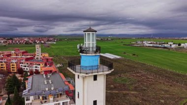 Drone, Bulgaristan 'daki canlı yeşil alanlara tepeden bakan bir deniz fenerinin nefes kesici manzarasını yakalıyor. Yakın binalar bulutlu bir gökyüzünün altındaki sakin manzarayı tamamlıyor.