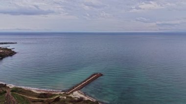 Bu büyüleyici hava sahnesi, Bulgaristan 'ın sakin kıyı şeridini ve bulutlu bir gökyüzünün altında denize uzanan kayalık bir iskeleyi gözler önüne seriyor..