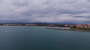 Sakin bir hava manzarası Bulgaristan 'ın manzaralı kıyı şeridini gösteriyor. Dalgalar yavaşça kıyıya vuruyor ve binalar kasvetli bir gökyüzünün altında su kenarını kaplıyor..