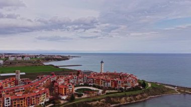 Bulgaristan 'da renkli binalar, deniz feneri ve bulutlu bir gökyüzünün altında ufka doğru uzanan deniz manzaralı bir kıyı bölgesini gözler önüne seriyor.