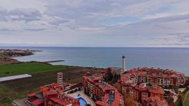 Bulgaristan 'da renkli binalar, yeşil tarlalar ve bulutlu bir gökyüzü altında sakin denizlerin yer aldığı güzel bir kıyı köyü görülüyor.