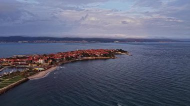 Bulgaristan 'ın Nesebar kentinin tarihi binaları, kıyı dalgaları ve dingin akşam gökyüzü boyunca canlı renklerini gösteren hava manzarası, ülkenin Nesebar kentinin güzelliğini yansıtıyor.