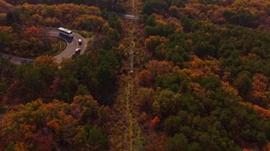 Bu hava manzarasında, Bulgaristan 'da sonbahar aylarında renkli bir ormanın içinden geçen dolambaçlı bir yol görülüyor. Ağaçlar turuncu, kırmızı ve yeşilin çarpıcı tonlarını sergiliyor..