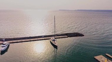 Güneş sakin suların üzerinde batarken, bir yelkenli, ufuktaki altın ışığı yansıtan Bulgar sahilindeki marinada huzur içinde dinleniyor..