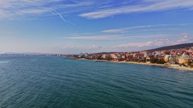 Canlı bir Bulgar kasabasının kıyı şeridi boyunca uzanan parlak mavi sular güneşli bir günde renkli binalar ve huzurlu bir plaj sergiliyor..
