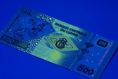 Mavi ışık altında 500 franklık bir banknot gösteriliyor. Tasarımda Kongo parasının tipik sembolleri ve desenleri yer alıyor..