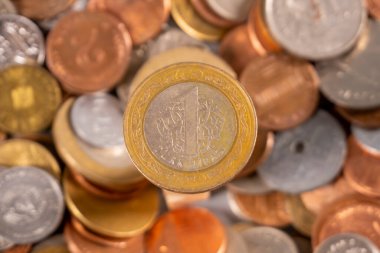 Birçok madeni para bir yüzeye saçılmıştır, ortada duran bir madeni para vardır. Bozuk paraların farklı boyutları ve renkleri var, çeşitli mezhepleri ve tasarımları gösteriyor..