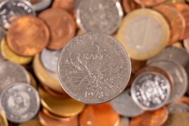 Yakın planda, farklı ülkelerden ve yıllardan gelen paralar arasında 5 frank madeni para yer alıyor. Sikkeler düz bir yüzeyde dağınık bir şekilde düzenlenir..
