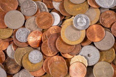 Birçok madeni para bir masanın üzerine saçılmıştır. Madeni paraların boyutları ve materyalleri, yerel bir pazarda toplanan çeşitli ülkelerden toplanan farklı tasarımları göstermektedir..