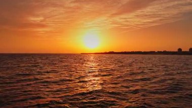 Bulgaristan 'ın Nesebar kentindeki sakin denizin üzerinde güzel bir günbatımı gökyüzünü aydınlatıyor. Güneş batarken dalgalar yavaşça dalgalanır ve kıyı manzarasının huzurlu bir görüntüsünü oluşturur..