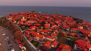 Nesebar deniz kenarındaki büyüleyici kırmızı çatılı evlerini gösteriyor güneş ufukta batarken, bu tarihi kasabanın üzerinde gökyüzünde güzel bir renk karışımı oluşturuyor..