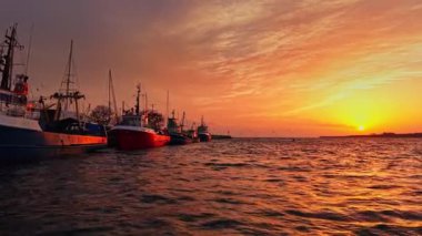 Bulgaristan 'ın Nesebar kentinde güneş batarken balıkçı tekneleri limana yanaşıyor. Gökyüzü turuncu ve pembe renklerle parlayarak, suda sakin bir akşam atmosferi yaratır..