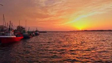 Bulgaristan 'ın Nesebar kentindeki liman üzerinde canlı günbatımı sıcak renkler oluşturuyor. Balıkçı tekneleri kıyıya yanaşıyor, sakin bir deniz manzarası yaratıyor..