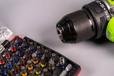 Matkap ve tornavida ucu gri bir yüzeyde gösteriliyor. Aletler bir ev geliştirme projesi sırasında kullanılmaya hazırdır. Yakınlardaki bir vakada çeşitli parçalar düzenlenir.